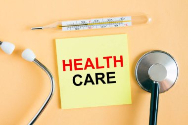 Sağlık Hizmetleri yazılı sarı etiket. Sıcak bir arka planda fonendoskoplu bir termometre. Tıbbi konsept fotoğrafı olarak kullanılabilir.