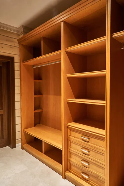 Luxury wardrobes in the dressing room with roll-out metal shelves. Cabinets made of alder veneer and alder wood