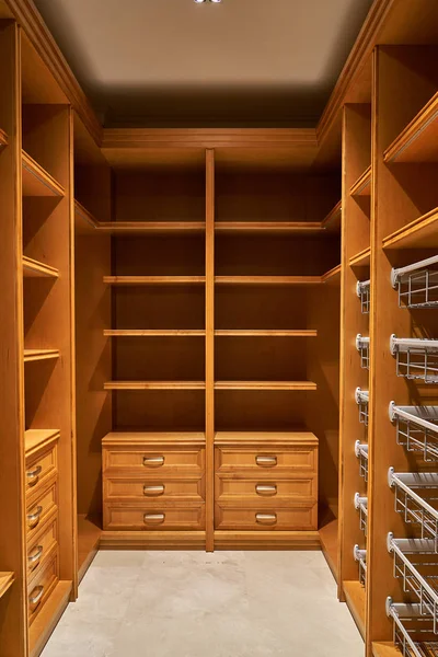Luxury wardrobes in the dressing room with roll-out metal shelves. Cabinets made of alder veneer and alder wood