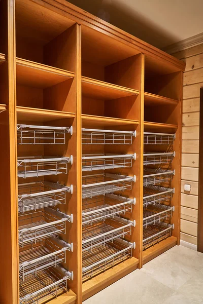 Luxury wardrobes in the dressing room with roll-out metal shelves. Cabinets made of alder veneer and alder wood