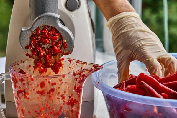 Making red hot chili pepper mash in a grinder. Hot sauce production.