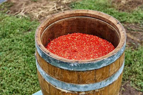 Open wooden barrel filled with milled hot pepper. Hot sauce production. Wooden barrel covered with wax on the background of green grass