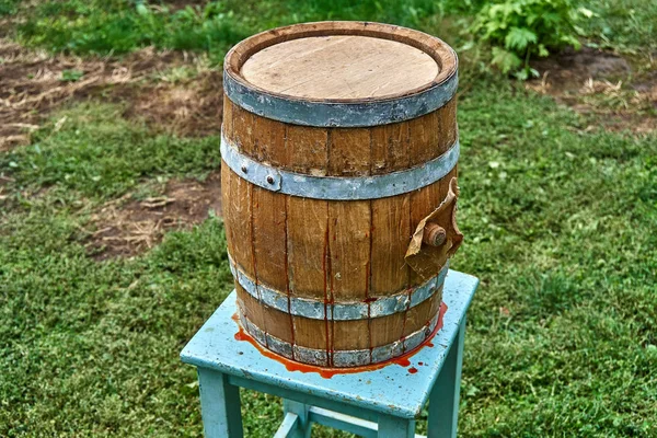 Wooden barrel. Hot sauce flows through the gap. Hot sauce production. Wooden barrel covered with wax on the background of green grass