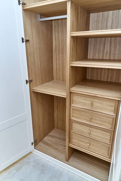 Opened white wardrobe with wooden drawers and shelves. Wooden filling of wardrobe. Wooden wardrobe with white lacquered cabinet doors