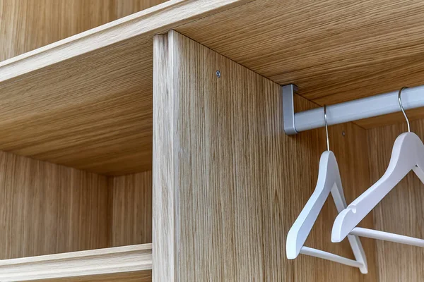 Opened white wardrobe with wooden shelves. Wooden filling of wardrobe and white clothes hangers. Wooden wardrobe with white lacquered cabinet doors