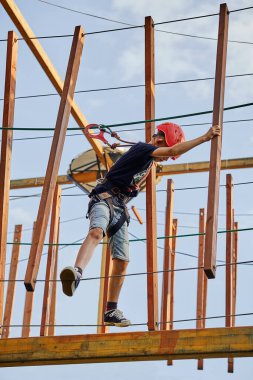 Miğferli ve tırmanma ekipmanlı bir çocuktan İp parkında zaman geçirirken iplerin üzerinde yürümeye