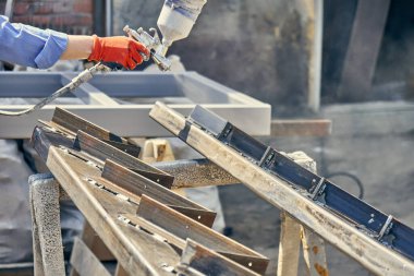Koruyucu kostümlü, eldivenli, sprey tabanca kullanan ve metal merdiven tellerini boyayan tanınmamış bir erkek işçi.