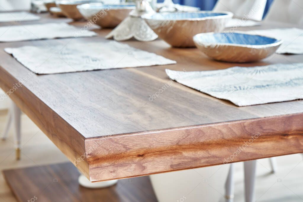Detail of dinner table made of solid walnut wood on massive legs and served with plates. Blurred background