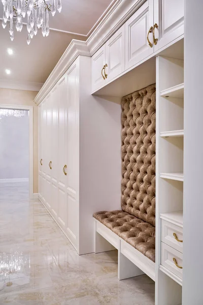 Classic white wardrobe with seating and shelves in contemporary bright hallway. Classic furniture. Carriage coupler closet bench
