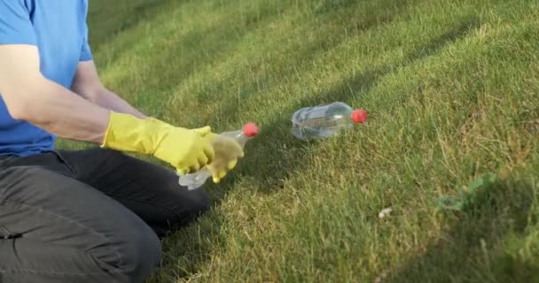 一个戴黄色手套的男人 从绿草上倒垃圾 扭动并挤压塑料瓶 以便日后进行分类 — 图库视频影像