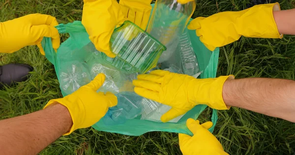 Sarı eldivenli eller poşette plastik döküntüler topluyor..