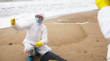 Beyaz koruyucu giysili bir bilim adamı, meslektaşına biyolojik tehlike içerikli bir fıçının yanında alınan örneklerin bulunduğu bir test tüpü gösteriyor..