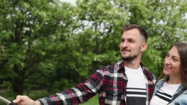 Mutlu genç çift parktaki yeşil ağaçların arka planında ortak bir selfie çekiyor..