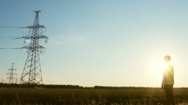 Koruyucu kasklı ve yeşil sinyal yelekli bir adam elektrik hattına bakıyor..