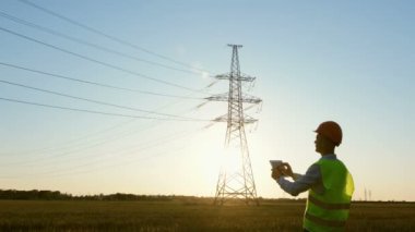 Özel elbiseli bir enerji mühendisi, tabletteki elektrik sensörlerinden elde edilen verileri kullanarak bir elektrik hattını denetliyor..