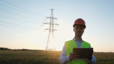 Güç sahibi bir adam elinde tabletle yüksek gerilimli bir elektrik hattının içinden geçer ve yüzünü çevirir..