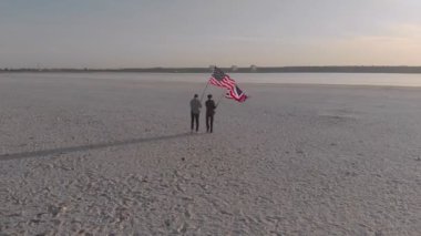 İki adam, Birleşik Devletler ve Büyük Britanya bayraklarıyla bayrak direkleri dikti, yan yana durdular ve göle doğru sarıldılar. Havadan çekim yapmak..