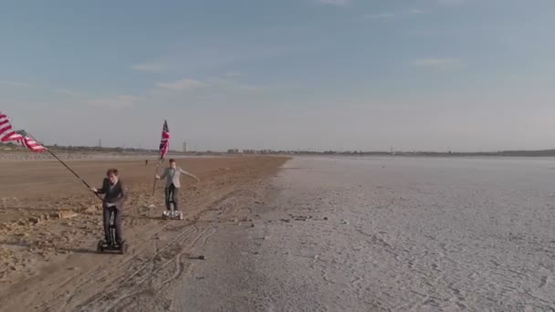 两个拿着美国和英国国旗的男子 一个接一个地沿着干涸的湖岸骑着马 英国正在努力赶上美国 — 图库视频影像