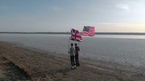 两个拿着美国和英国国旗的男人在海湾边骑摩托车 — 图库视频影像