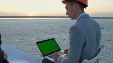 İş kıyafetleri ve turuncu kasklı iki adam Birleşik Krallık bayrağının altındaki boş bir alanda sandalyelerde oturuyorlar. İnşaat planı tartışılıyor. Gayrimenkule yatırım.