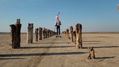 Adamın biri ıssız bir plajda Amerikan bayrağı taşıyan bir scooter kullanıyor. Bağımsızlık Günü yaklaşıyor..
