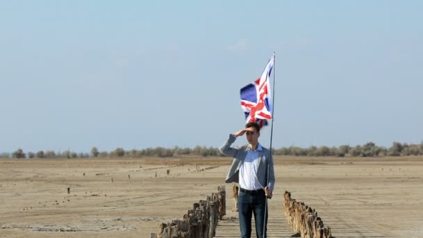 Парень Костюме Стоит Пустынном Берегу Британским Флагом Размахивающим Ветром Смотрит — стоковое видео
