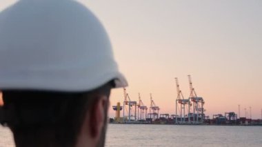 Adam kafasına beyaz koruyucu bir miğfer geçirir ve radyoda limanın arka planına karşı konuşur..