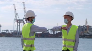 Yüz maskeli mühendisler limanın zeminine, karantina sırasında iki adamın selamlanmasına ve limanda lojistik gelişime karşı çalışıyorlar..
