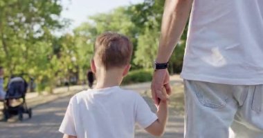 Anaokulu çocuğu olan bir adam kaldırımlı park yolunda yürüyor. Küçük çocuk, babasının elini sıkıca tutuyor. Diğer elinde bisiklet tutan uzun boylu yetişkin figürünün yanında yavaşça yürüyor.