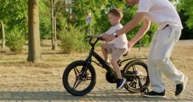 Küçük çocuk bisiklet sürerken baba bisiklet koltuğunda oturur ve dengeyi kurmayı öğrenir. Pedallar ileri doğru ilerlerken çocuk gidonu sıkıca kavrarken başarılı olma azmi gösteriyor