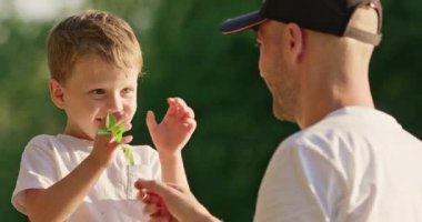 Babam okul çağındaki çocukla parkta yürürken küçük bir dal kullanarak oynuyor. Sarışın genç oğlan, gün batımında yüksek sesle gülüyor ve ince dallara hafifçe vuruyor.
