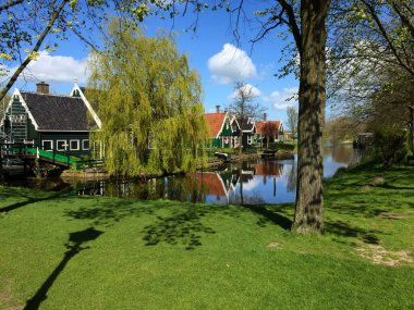Zaanse Schans, Kuzey Hollanda, Hollanda 'da mavi gökyüzüne karşı köy ve nehir manzarası