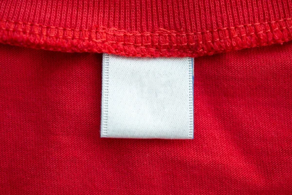 White blank clothing tag label on new red cotton shirt fabric texture background