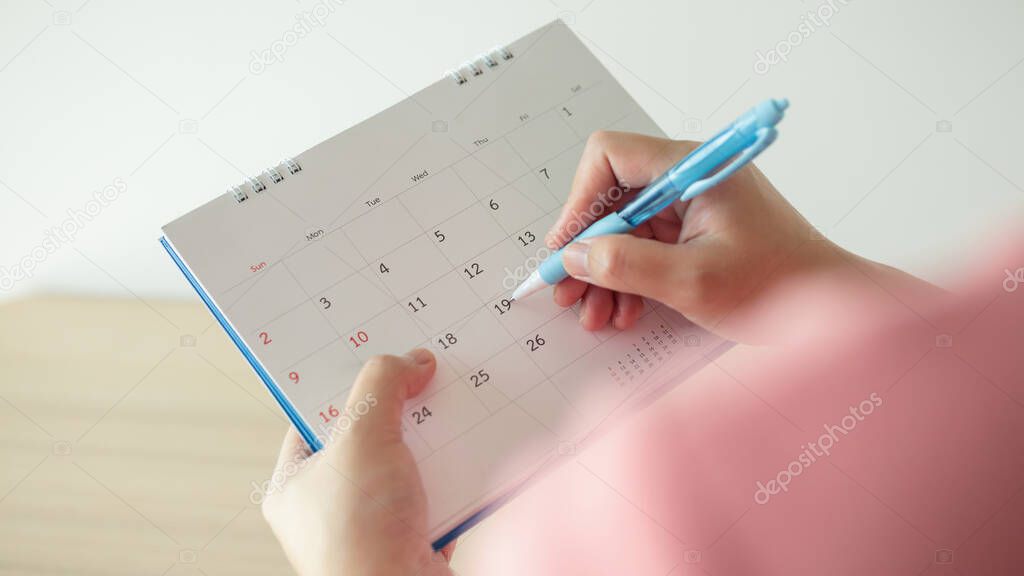 Hand with pen writing on calendar date