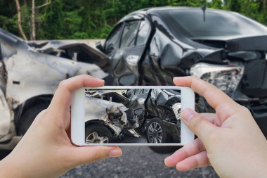 Akıllı telefon kullanan bir kadın trafik kazasının fotoğrafını çekiyor.