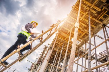 Genç profesyonel mühendis koruyucu miğfer ve bina inşaatında merdiven üzerinde çalışan planlar üzerinde çalışıyor.