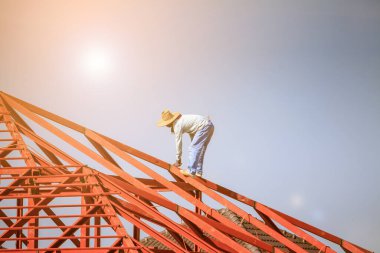 İnşaat işçileri binanın çatısının çelik iskelet yapısını inşa ediyorlar. İnşaat alanında bulutlar ve gökyüzü var.