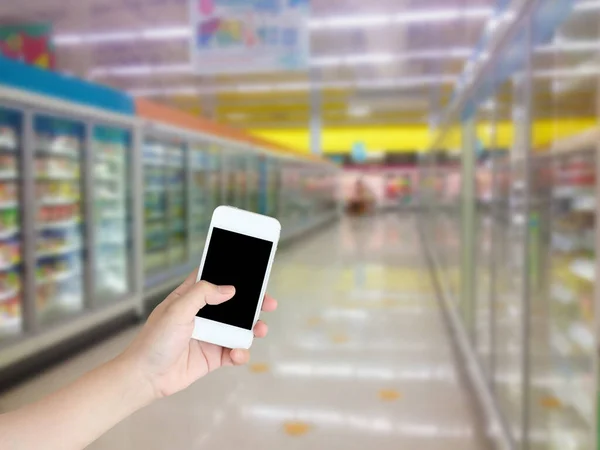 hand holding smartphone with Supermarket Aisle Milk Yogurt Frozen Food Freezer and Shelves blurred background