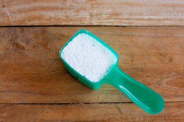 Ahşap arka plandaki ölçü kaşığında deterjan tozu.