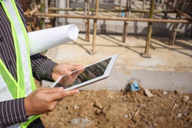 Asyalı işadamı inşaat yöneticisi ve koruyucu miğfer mühendisi inşaat alanındaki tablet bilgisayarı kullanarak proje taslaklarını ellerinde tutuyorlar.