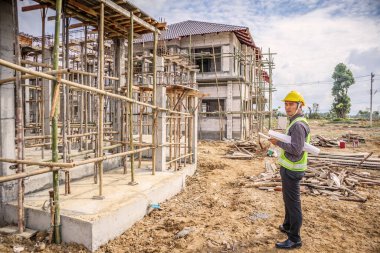 Asyalı işadamı inşaat yöneticisi ve koruyucu miğfer mühendisi inşaat alanındaki tablet bilgisayarı kullanarak proje taslaklarını ellerinde tutuyorlar.