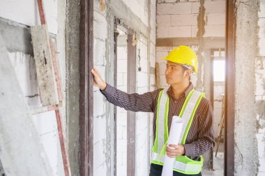 Asyalı işadamı inşaat mühendisi koruyucu miğfer ve bina inşaatında kullanılacak planlar.