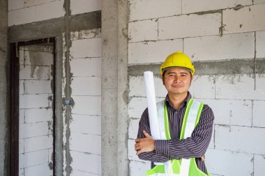 Asyalı işadamı inşaat mühendisi koruyucu miğfer ve bina inşaatında kullanılacak planlar.