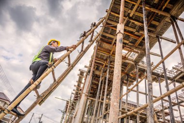Genç profesyonel mühendis koruyucu miğfer ve bina inşaatında merdiven üzerinde çalışan planlar üzerinde çalışıyor.