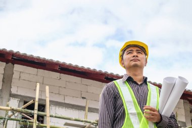 Asyalı işadamı inşaat mühendisi koruyucu miğfer ve bina inşaatında kullanılacak planlar.