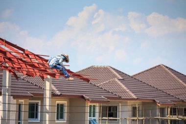 İnşaat işçileri binanın çatısının çelik iskelet yapısını inşa ediyorlar. İnşaat alanında bulutlar ve gökyüzü var.