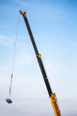 Mobil inşaat vinç kamyonunun sarı teleskopik kolları inşaat alanındaki inşaat alanına beton levha kaldırıyor.