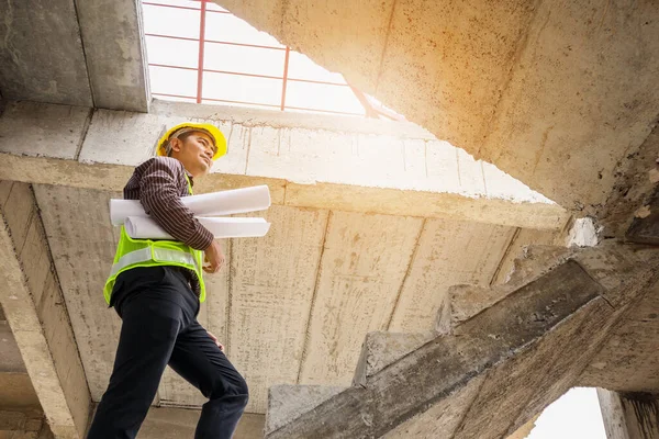 young professional engineer worker in protective helmet and blueprints paper on hand at the house building construction site