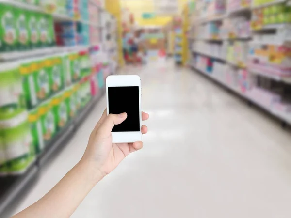 hand holding mobile phone with supermarket shelves aisle blurred background