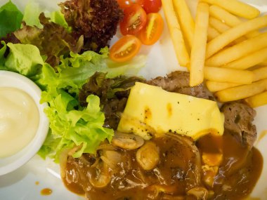 Peynirli ızgara biftek, yanında patates kızartması ve beyaz tabakta sebze.